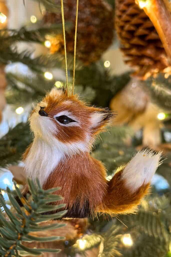 A furry fox sits inside the Christmas Tree with antlers and pine cones.