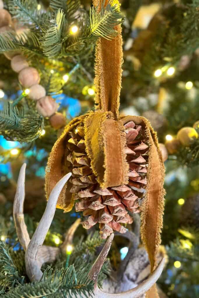 Pinecone ornament hanging in the Christmas tree with frayed edged gold velvet ribbon- decorating a tree in green and gold