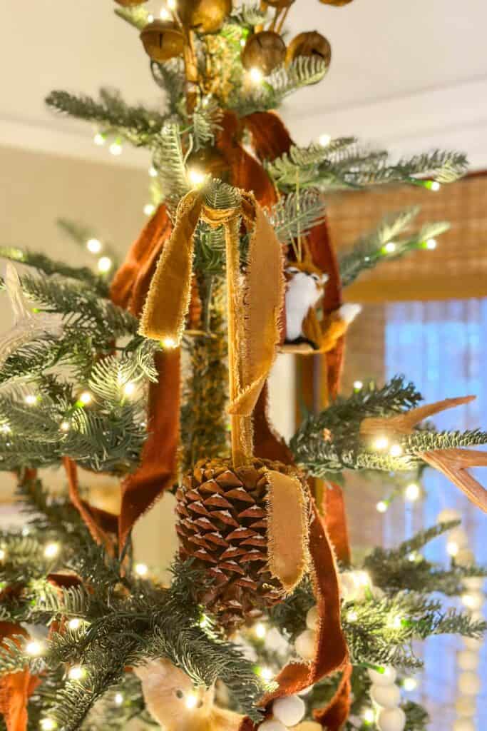 Velvet ribbon streaming down from the top of a Christmas tree with pinecones and rusty bells.