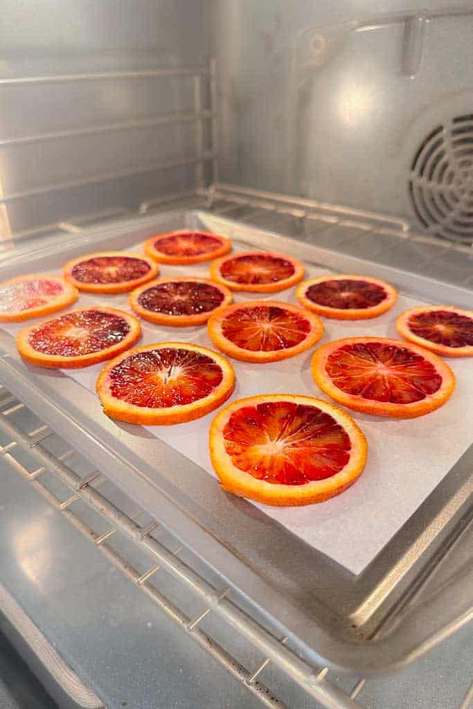 Blood orange sliced on parchment paper and a cookie sheet, in the oven.