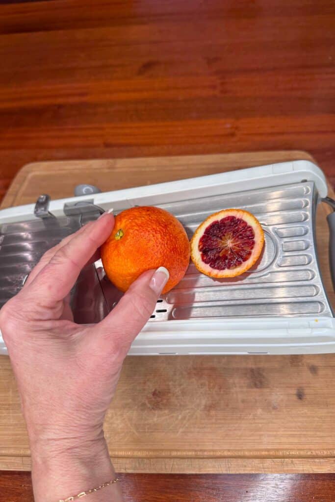 A woman slicing blood oranges on a mandoline to get even slices
