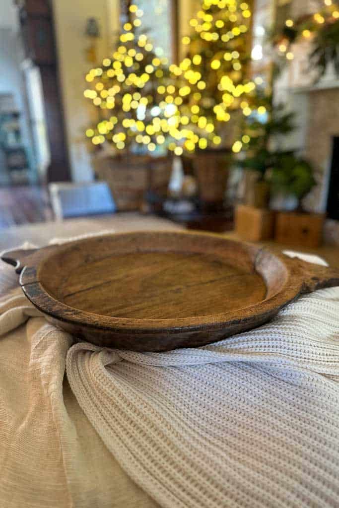 A wood tray sitting on an ottoman in the family room in the process of creating a vignette for Christmas.Two Christmas trees in the background.