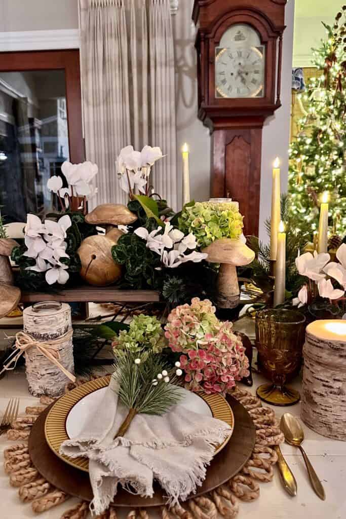 A rustic table setting for Christmas with a wooden sleigh decorated with fresh white cyclamen and wooden mushrooms.