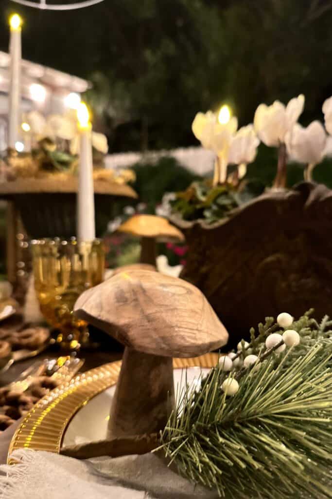 Wood mushroom sitting on a gold and white dinner plate with holiday greenery.