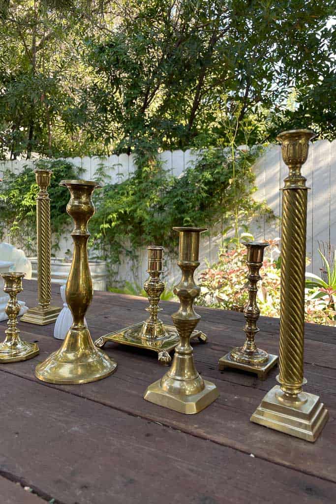 An assortment of brass candlesticks are getting ready to set a Christmas tablescape.