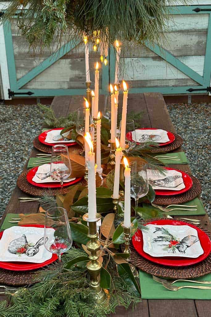 Outdoor rustic tablescape for Christmas with red and green decor. Fresh greenery and lots of white candles.