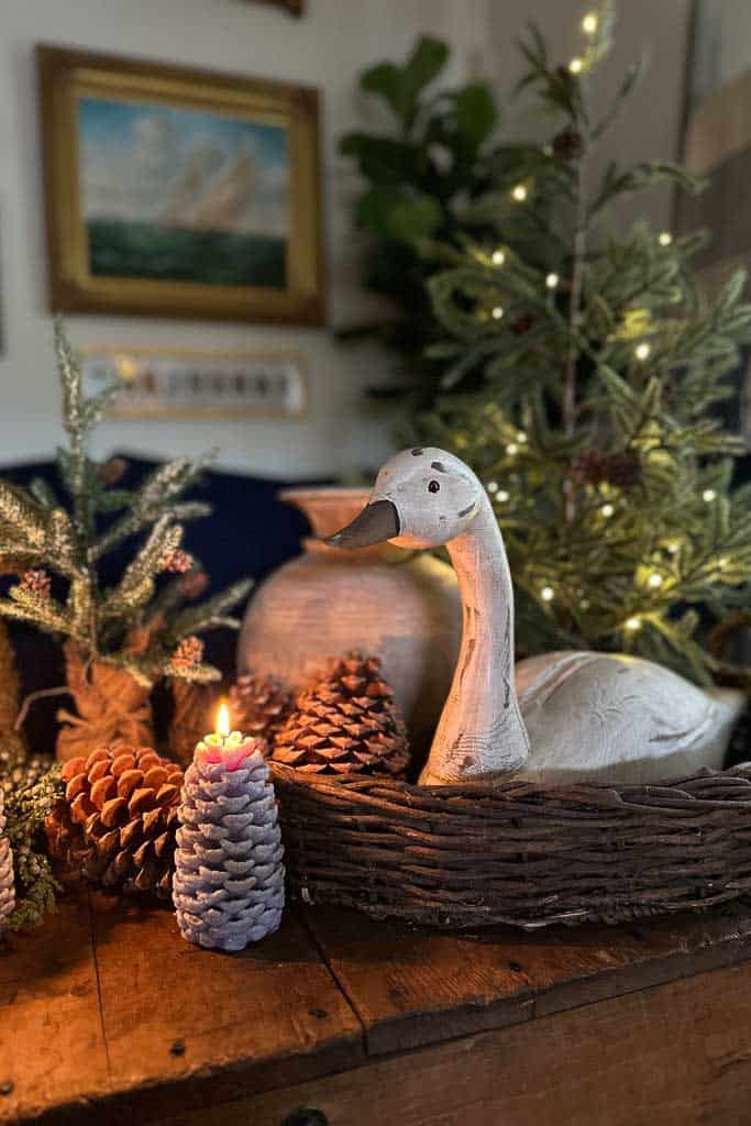 A round wicker basket filled with pine cones, a small Christmas tree, and a swan for Christmas.