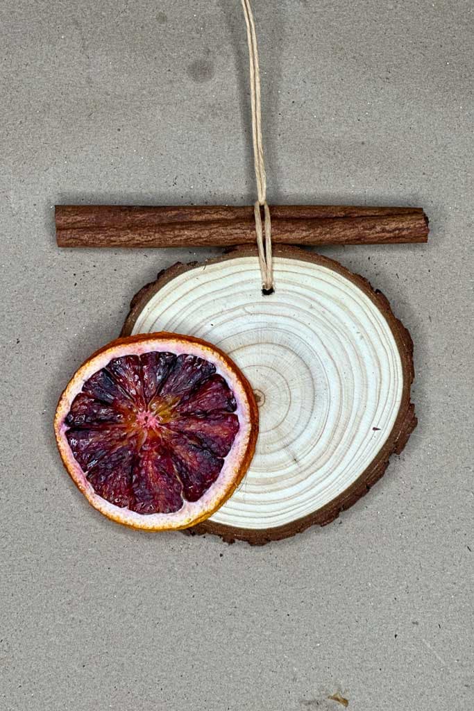 Small wood slices and cinnamon sticks are being used for ornament-making with dehydrated orange slices.