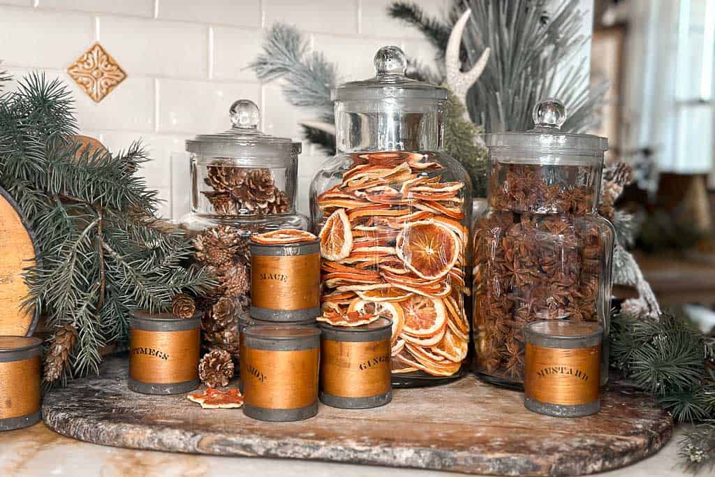 Apothecary jars filled with oranges, anise stars, and pinecones for Christmas.