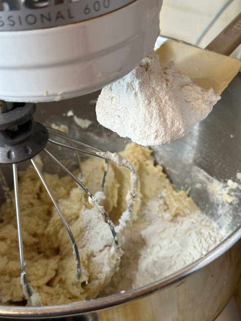 Christmas sugar cookies with sprinkles. In a kitchen aid mixer, we add flour to a sugar and butter mixer.