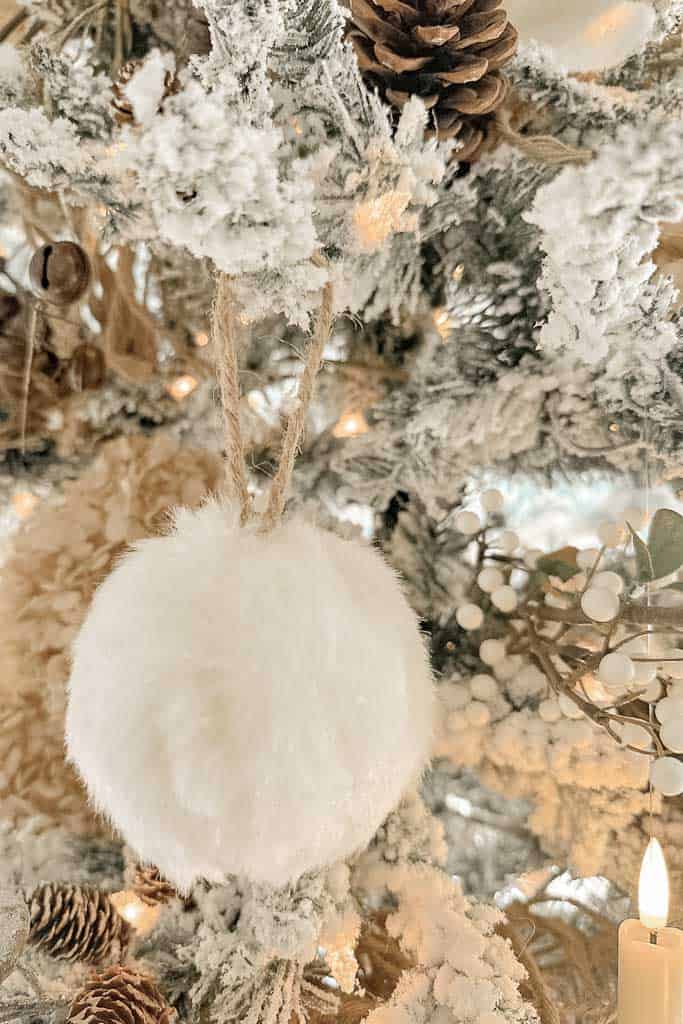 A white fur ball ornament hanging on the Christmas tree. 