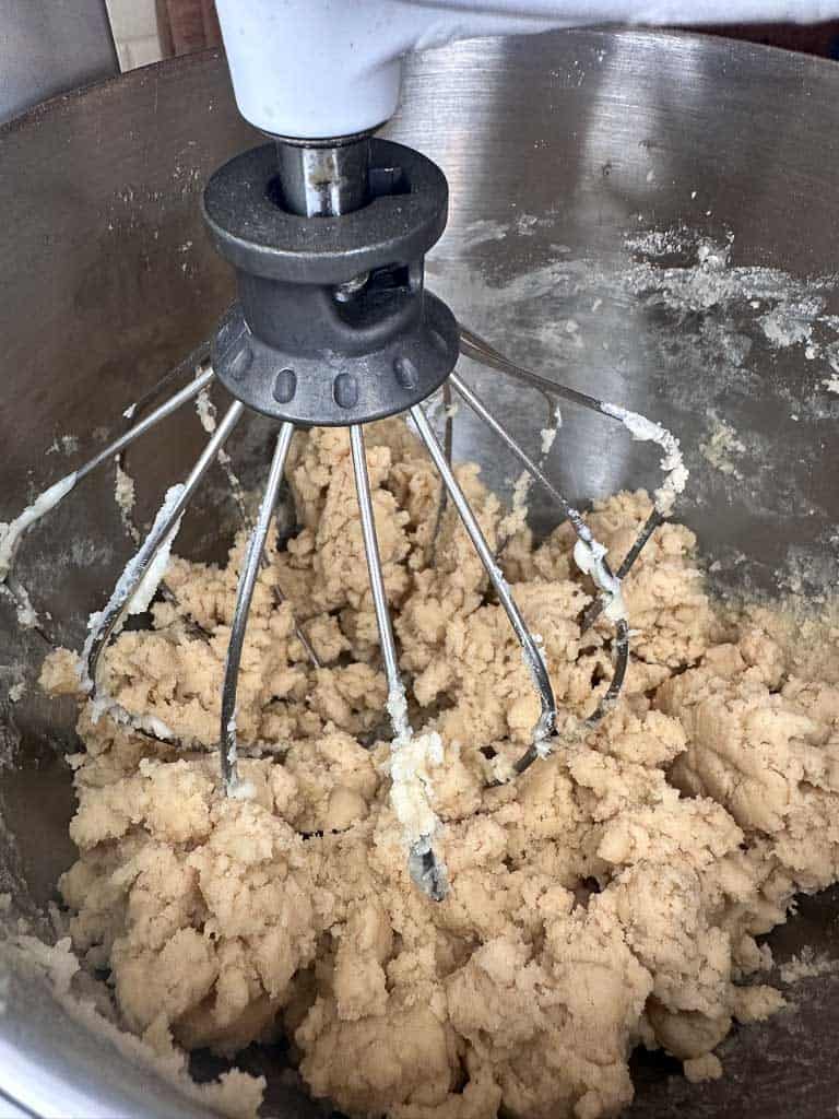 A kitchen aid mixture mixing butter, sugar, and flour mixture to make chewy sugar cookies with sprinklers.