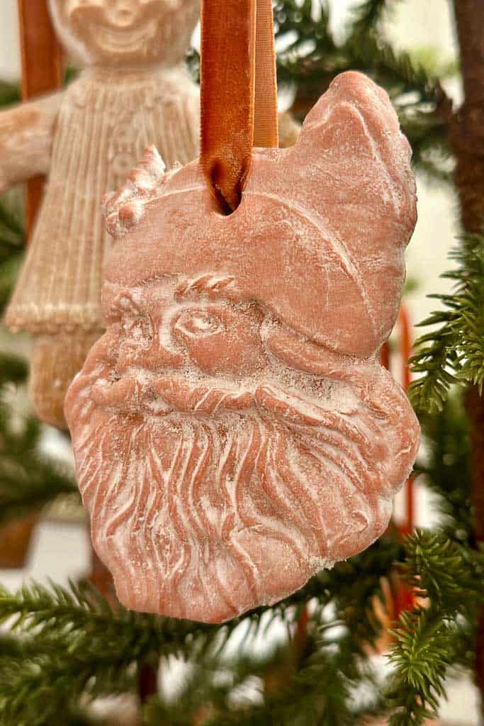 An air-dried terra cotta clay Santa Clause ornament hanging on the tree.