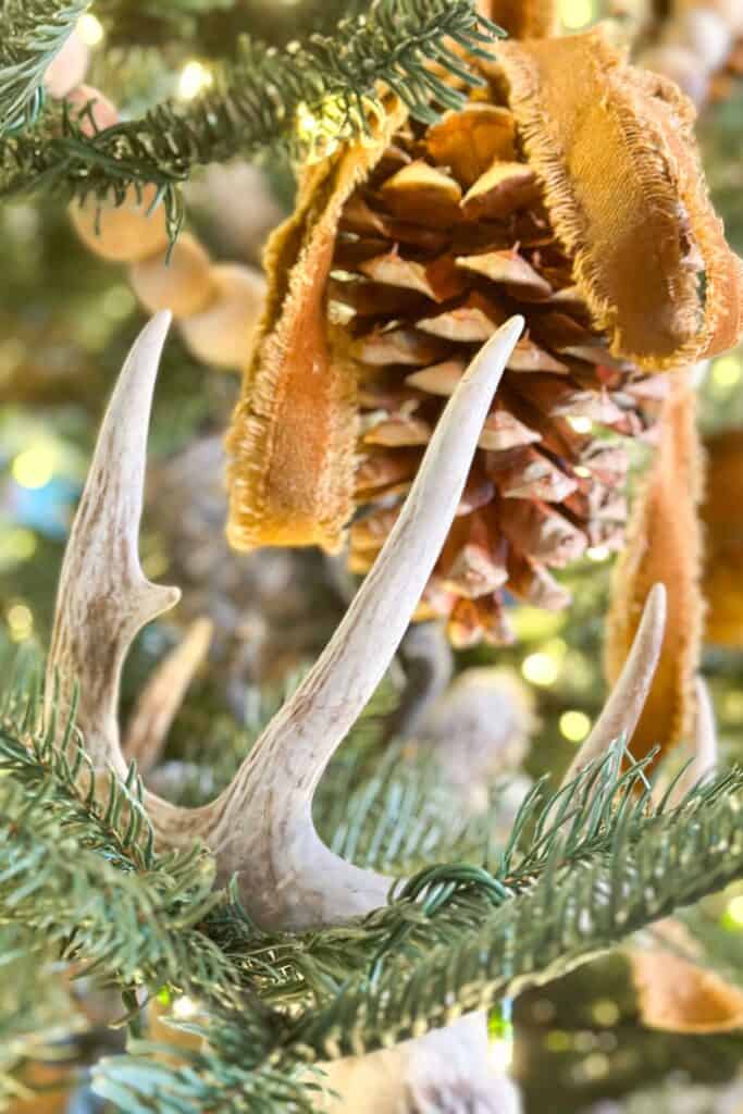 Antlers and pine cones in a Christmas tree draped with velvet ribbon.