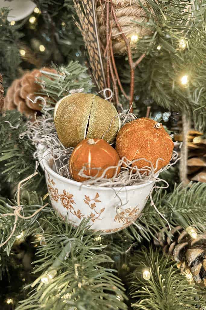 Whole dried oranges are placed in a teacup with moss hanging on the Christmas tree.