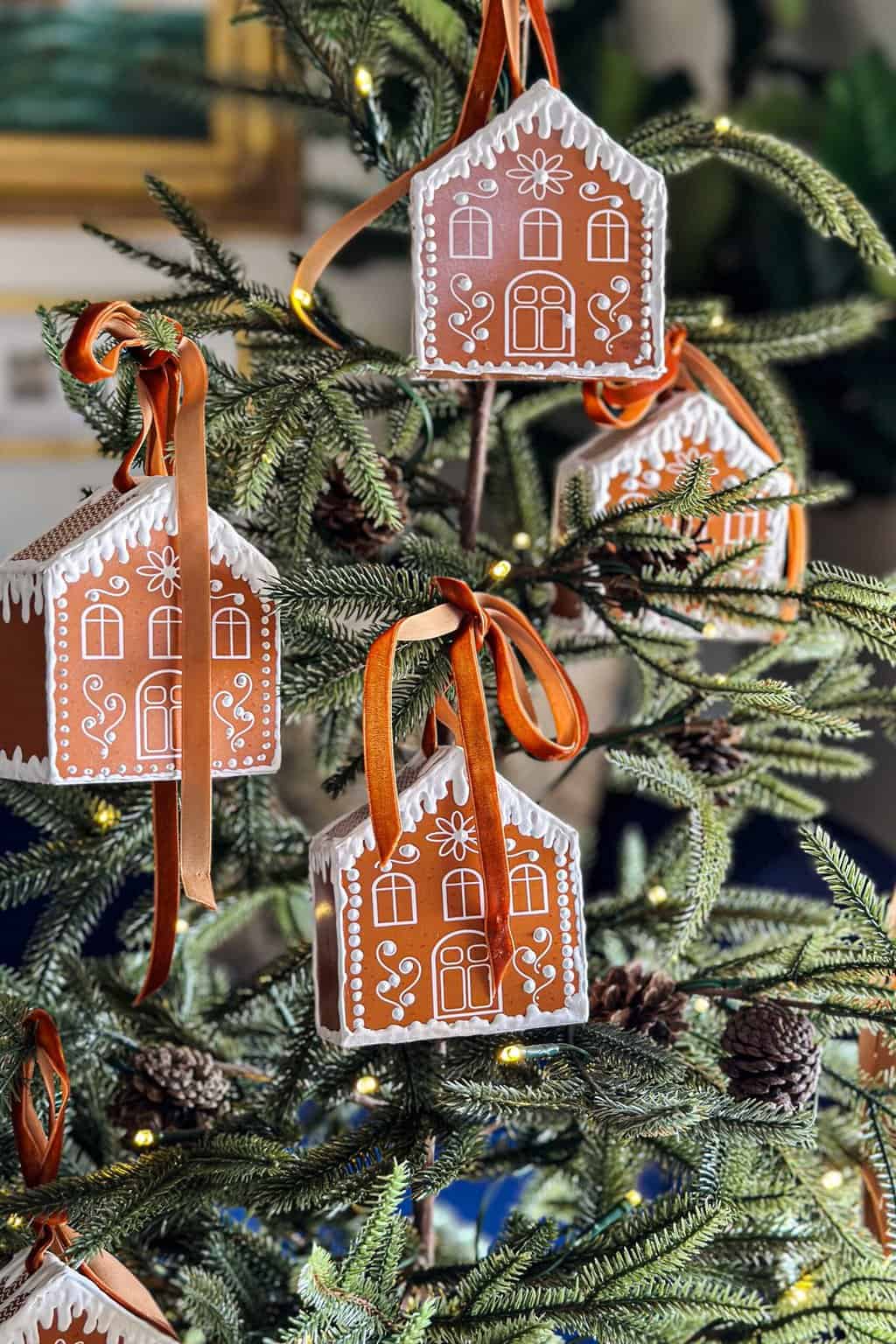 Four free printable 3D gingerbread houses with velvet ribbons hang on a small Christmas tree.