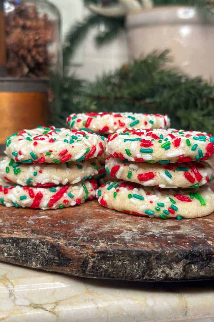 Stacked sprinkle Sugar Christmas cookies on a wooden platter.