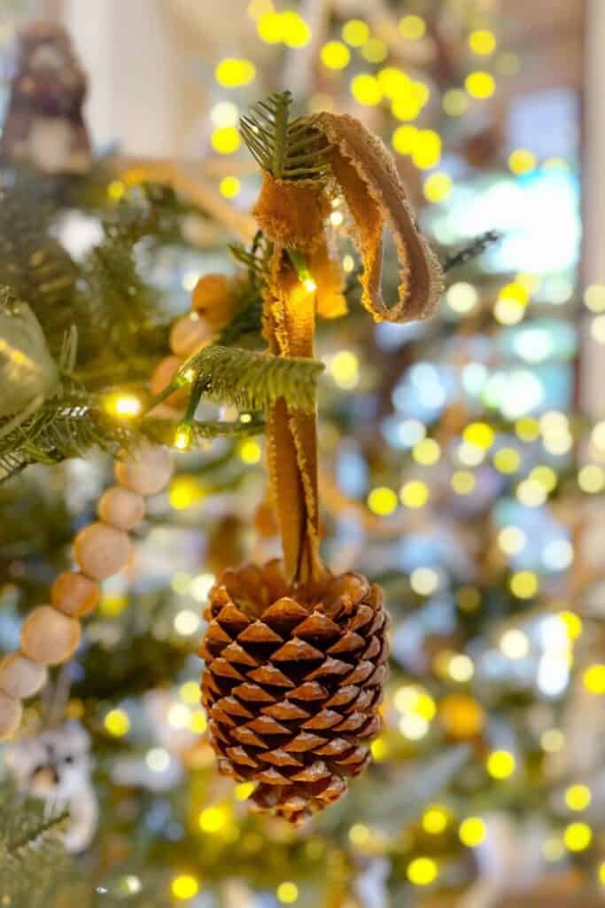 A natural pinecone hanging amongst the gold lights of a Christmas tree. 