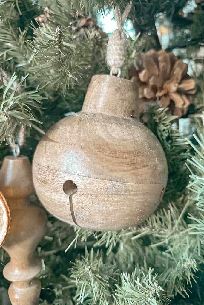 A wooden jingle bell ornament is hanging in the Christmas tree. 