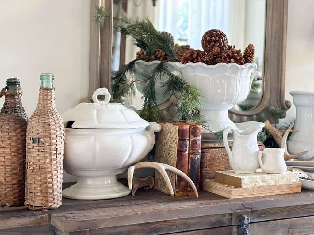 A Display of white ironstone on the dining room buffet with greenery, antlers, vintage books and pinecones.