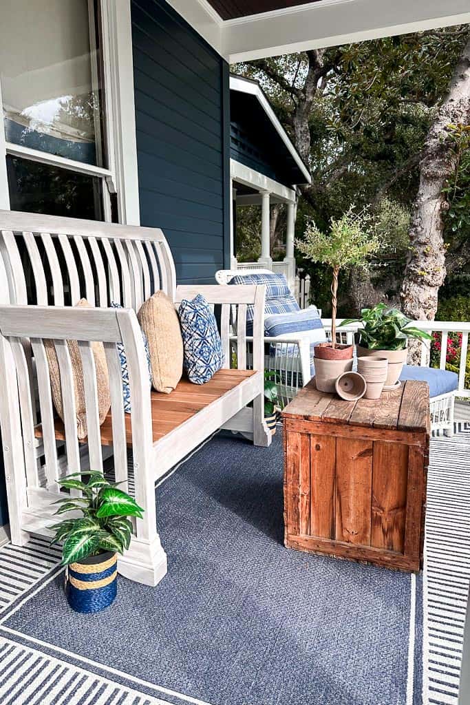 Blue and white front porch decor with a white bench and chair with a vintage box used as a coffee table. 