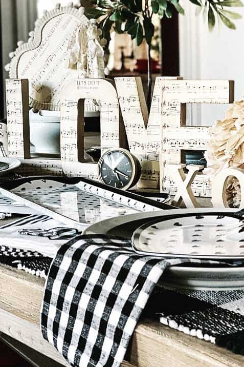 LOVE letters that are covered in music paper and used for a centerpiece on a black and white tablescape for Valentine's Day table.
