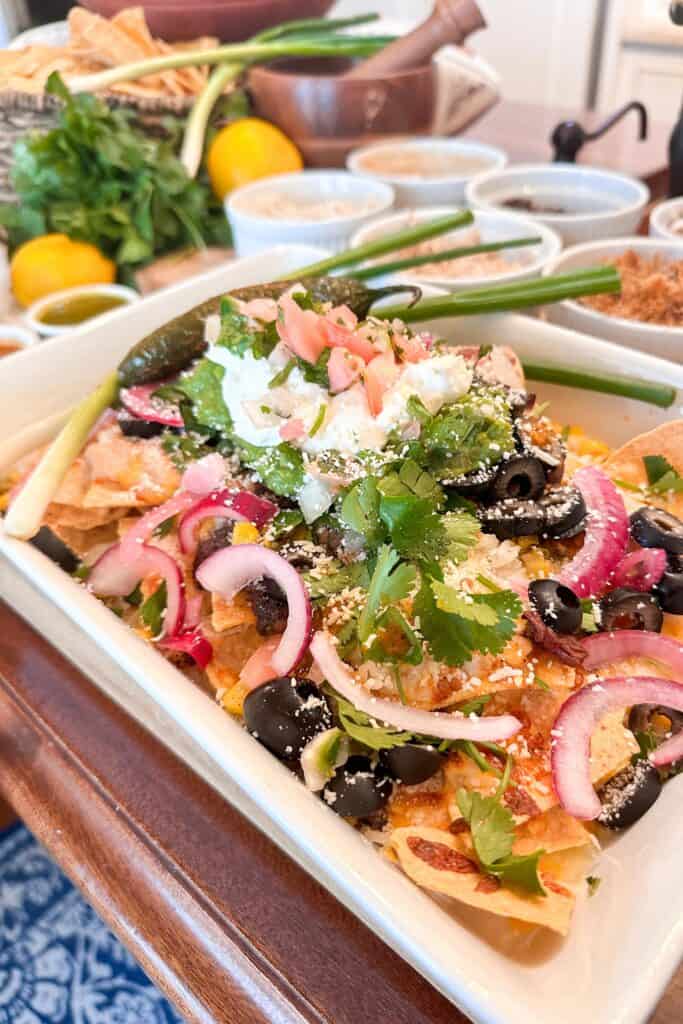 A tray of nachos from the 35 nacho toppings sits on the bar, including black olives, cilantro, chips, shredded chicken, sour cream, and more.