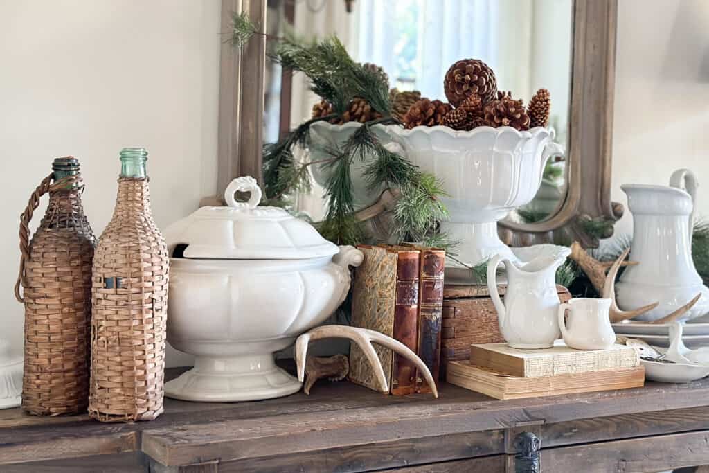A Display of white ironstone on the dining room buffet with greenery, antlers, vintage books and pinecones.