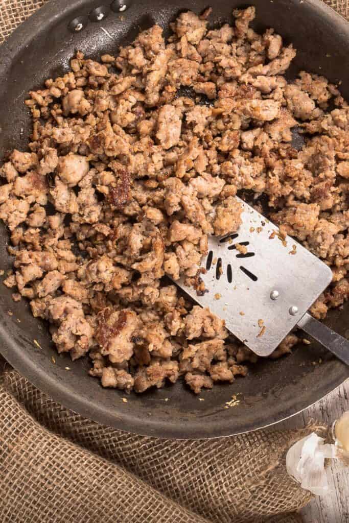 A pan full of sausage that is browning- 35 nacho toppings list.