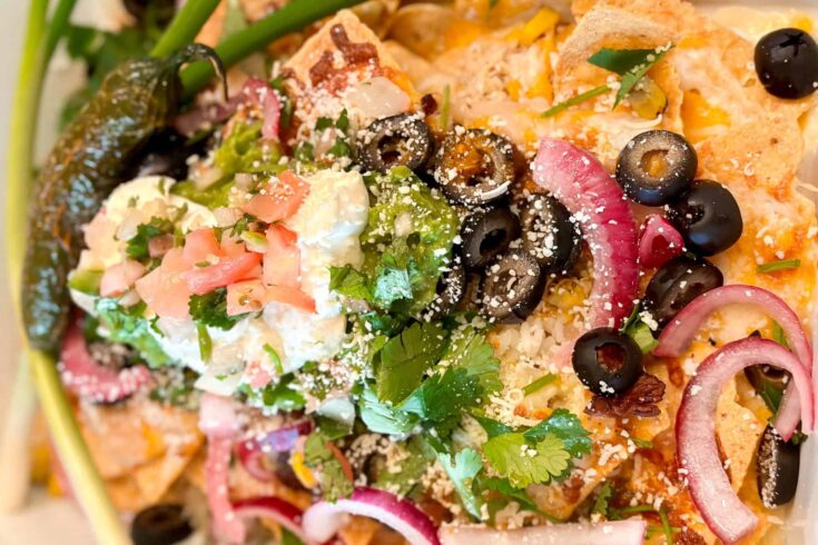 Game day nachos layered with chips, shredded chicken, cheese, pickled onions, guacamole, sour cream, black olives, and cilantro.