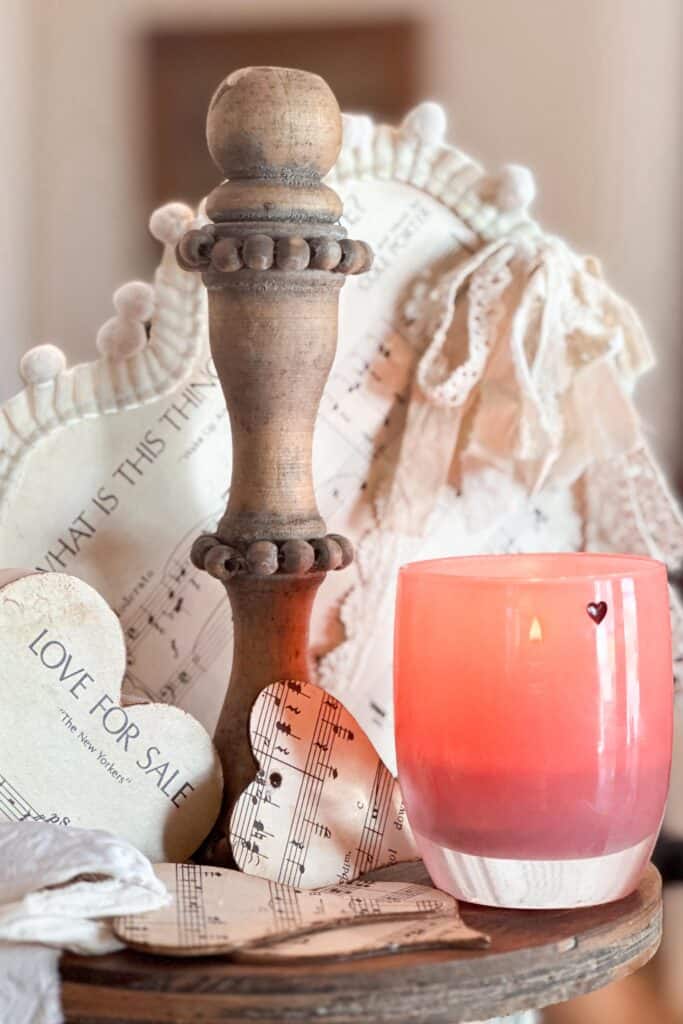 A pink candle is sitting on a tiered tray for some Valentine's Day decorations. 