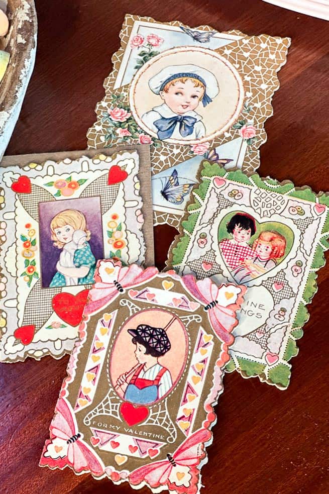 A collection of four vintage Valentine cards featuring illustrations of children. The cards have ornate borders, hearts, and floral designs. Each card showcases a different child in various sweet and tender poses.