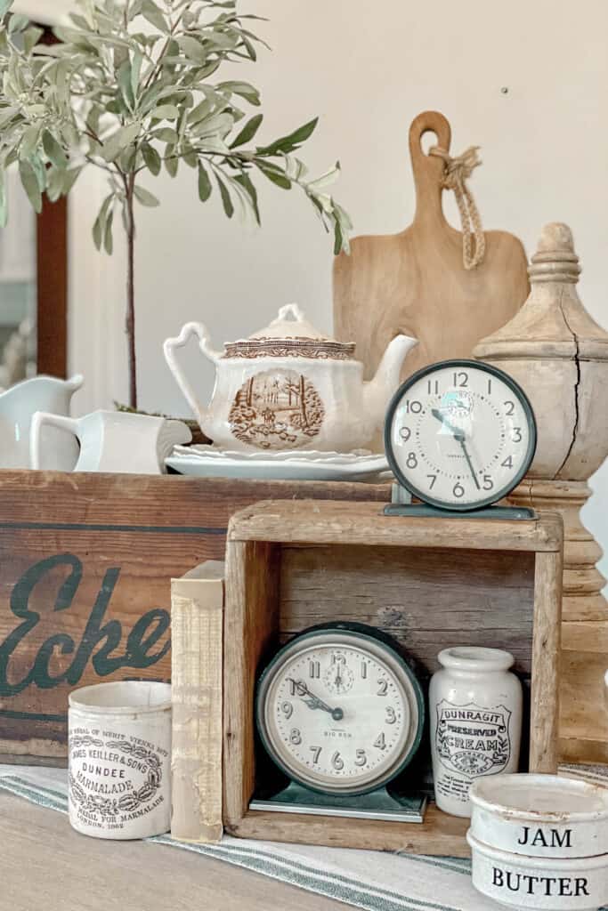 Weathered wood crates overflow with white ironstone pitchers and bowls, holding winter greenery and wood pieces: vintage clocks and more for a winter tablescape.