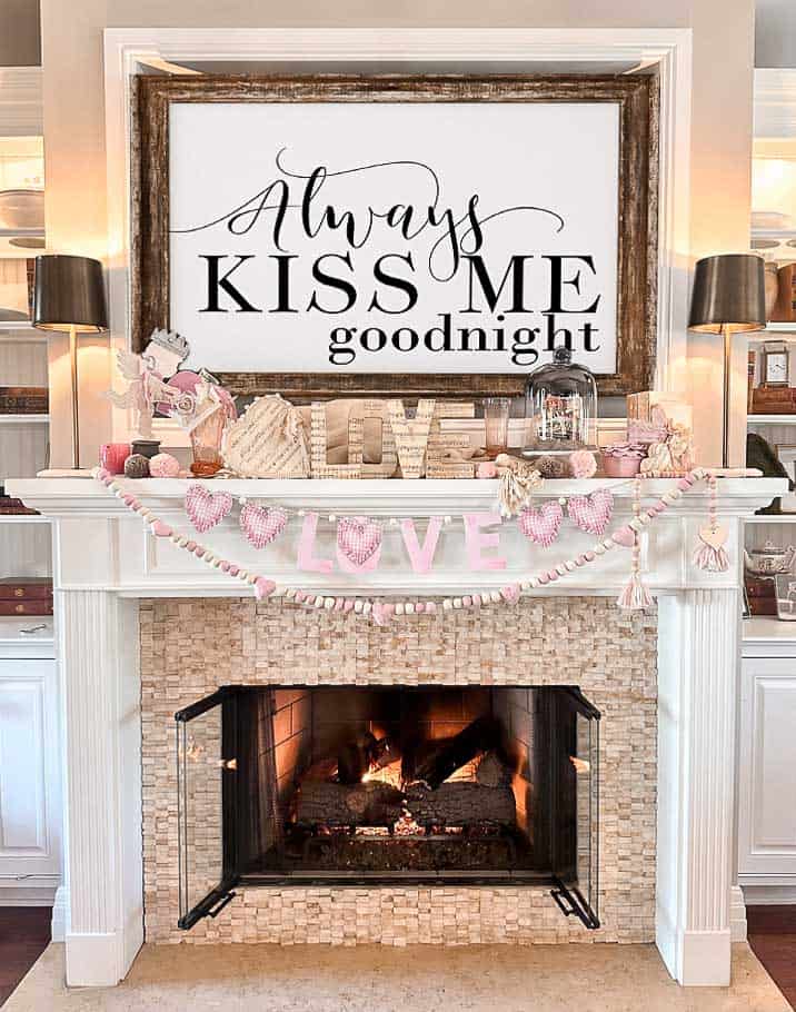The fireplace mantel is set for Valentine's Day with a sign above. A darling pink "LOVE" free printable banner hangs before the fireplace.