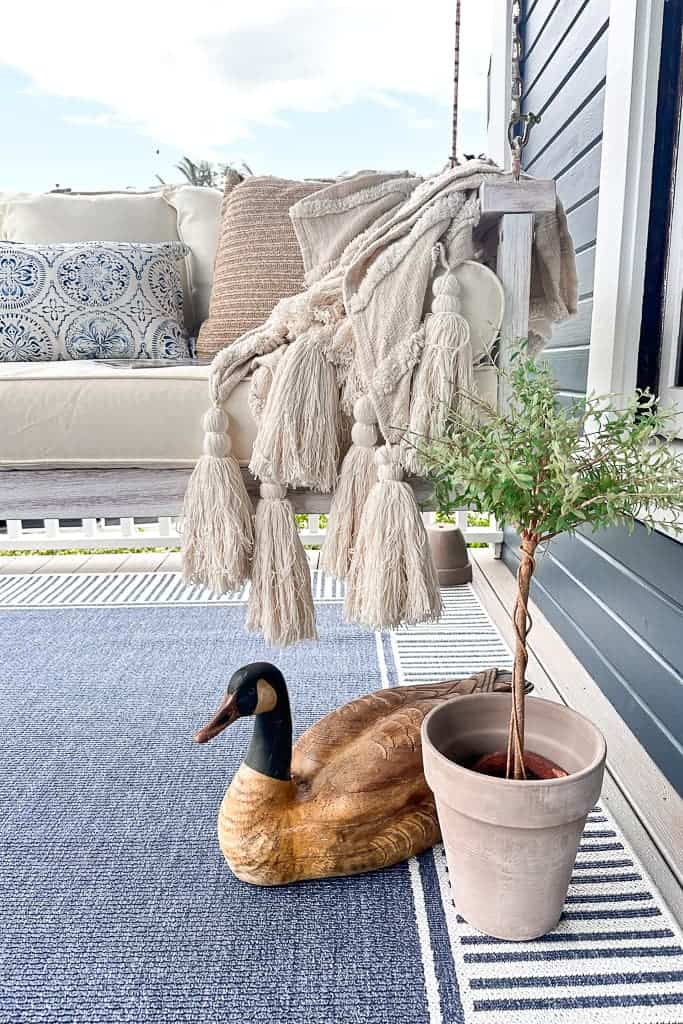 Vintage wooden goose and topiary sit on the front porch. Both of these items were purchased at an estate sale for a very low cost. A fringed throw on the swing adds great texture.