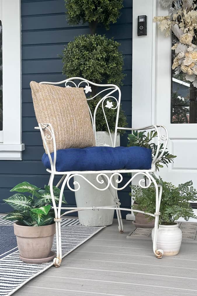 Vintage white metal chair with throw pillows and plants around the edges.