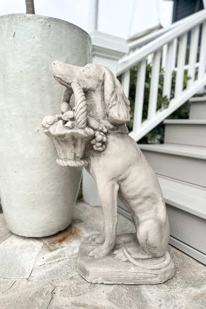 Cement dog with a basket of flowers in his mouth sitting on the front porch