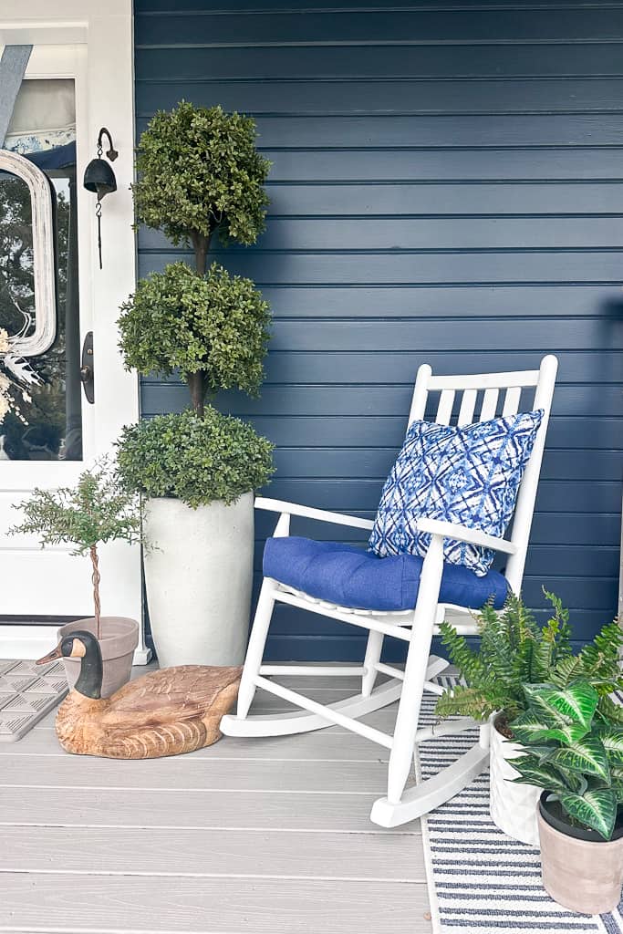 White rocking chair with a blue cushion sitting on the front porch 