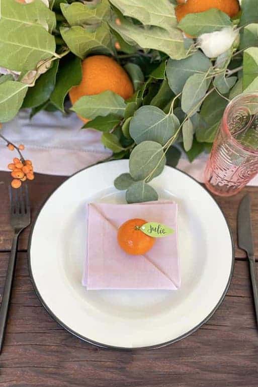 A table set for a little cutie tablescape with a floral and orange centerpiece. Little cuties are used for the name cards.
