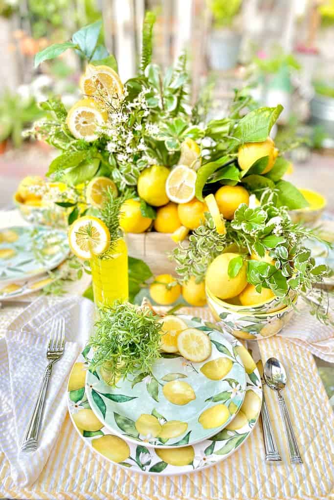 Outdoor dining table set with a lemon theme. The centerpiece is made of greens and fresh lemons with cute lemon plates and yellow glasses. 