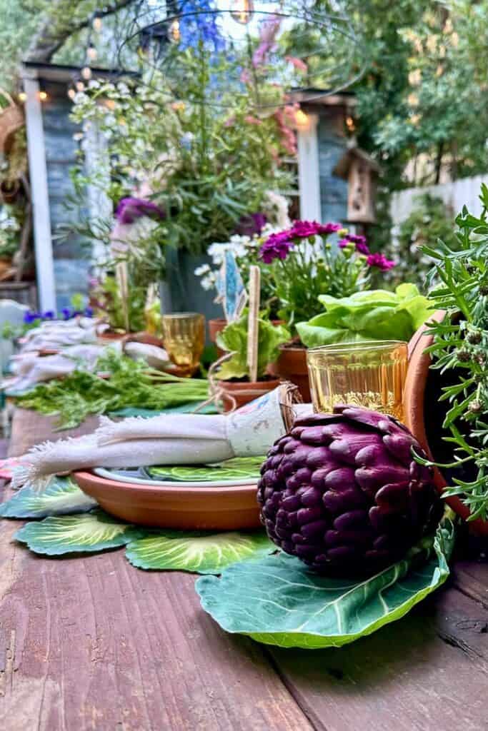 This is an up-close view of the vegetables featured in this garden party tablescape. Lots of fresh greenery, vegetables, and flowers adorn the table set with terra cotta saucers and linen napkins. 