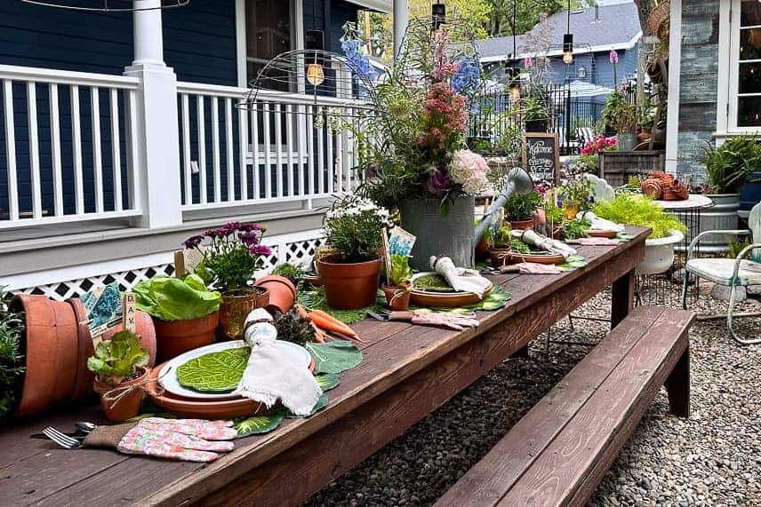 A large farm table is set with garden-themed decor, including terra cotta pots, a galvanized watering can, gardening gloves, and more. 
