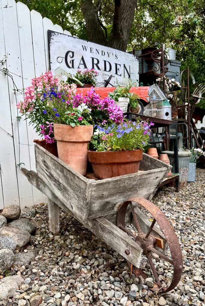 A wooden vintage wheelbarrow filled with terra cotta pots and springtime flowers.