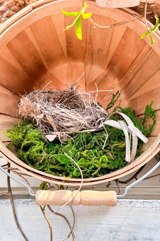 A wooden basket with green moss and a small birds nest. 