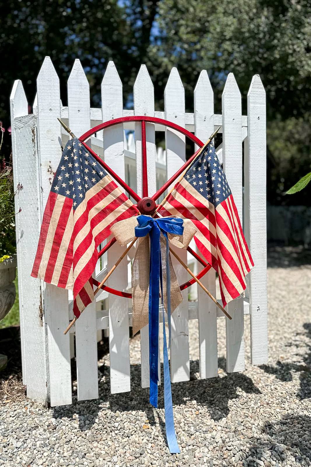 DIY patriotic wagon wheel wreath with American flags hanging on a picket fence