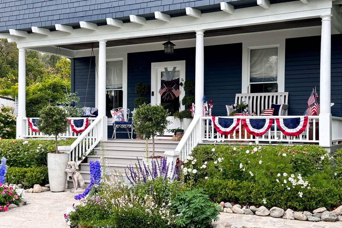 A blue house with a red white and blue porch decorated for the fourth of July.
