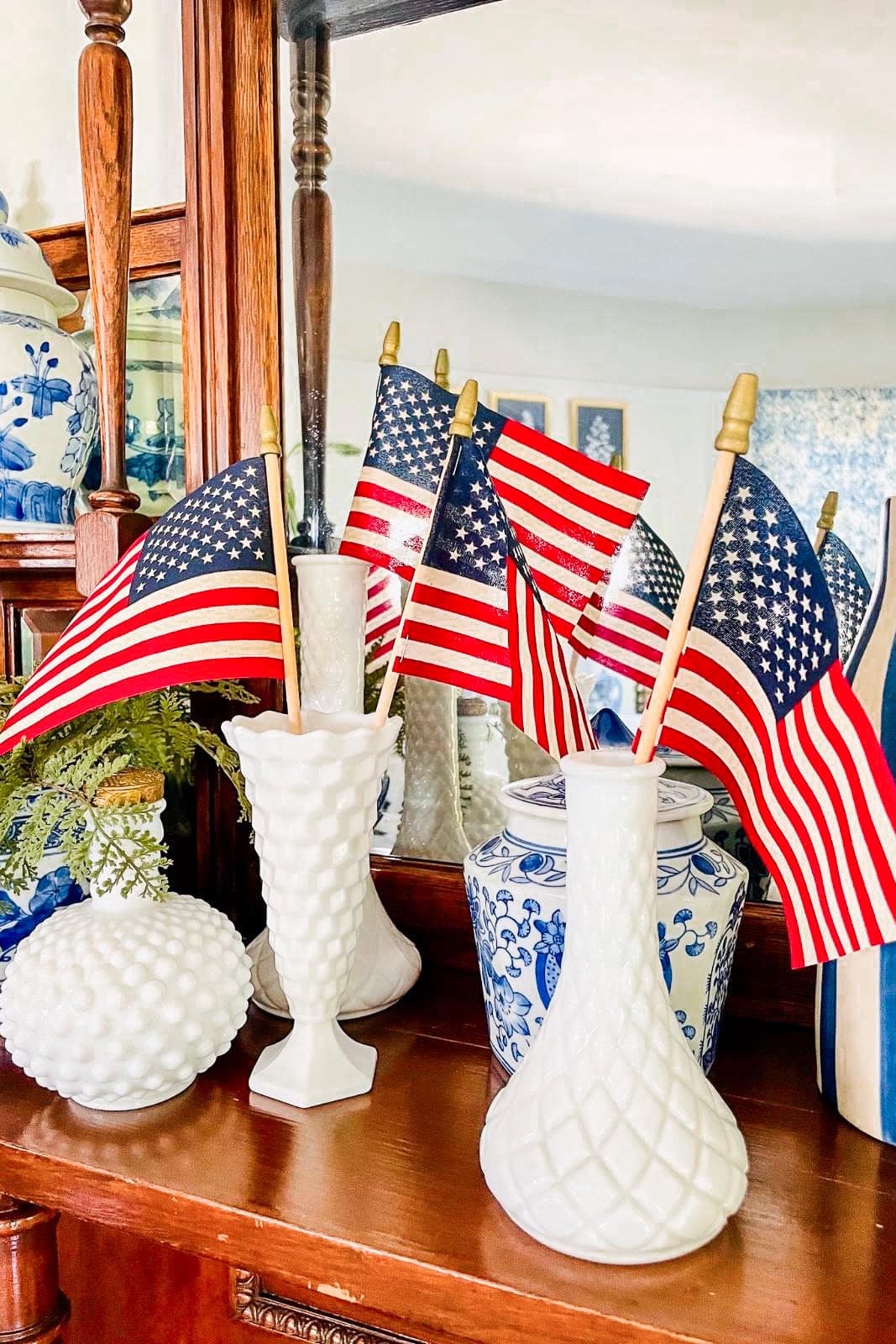 Close up view of American Flags displayed in a collection of milk glass vases on the fireplace mantel