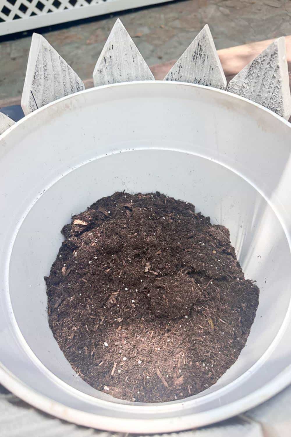 Soil inside of a flower pot with white pickets around the outside.