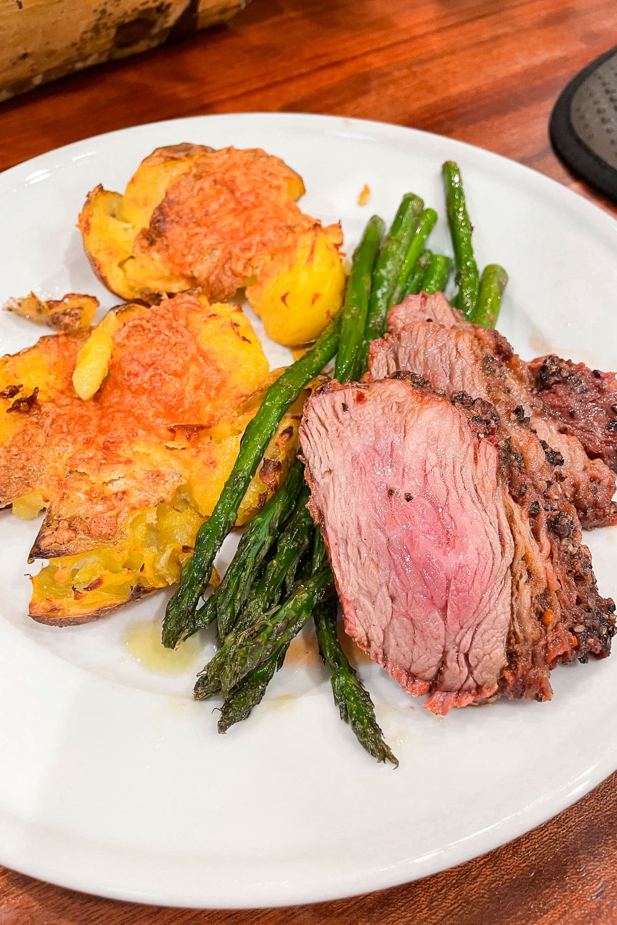 A Dinner plate filled with sliced smoked tri tip, asparagus and smashed potatotes.