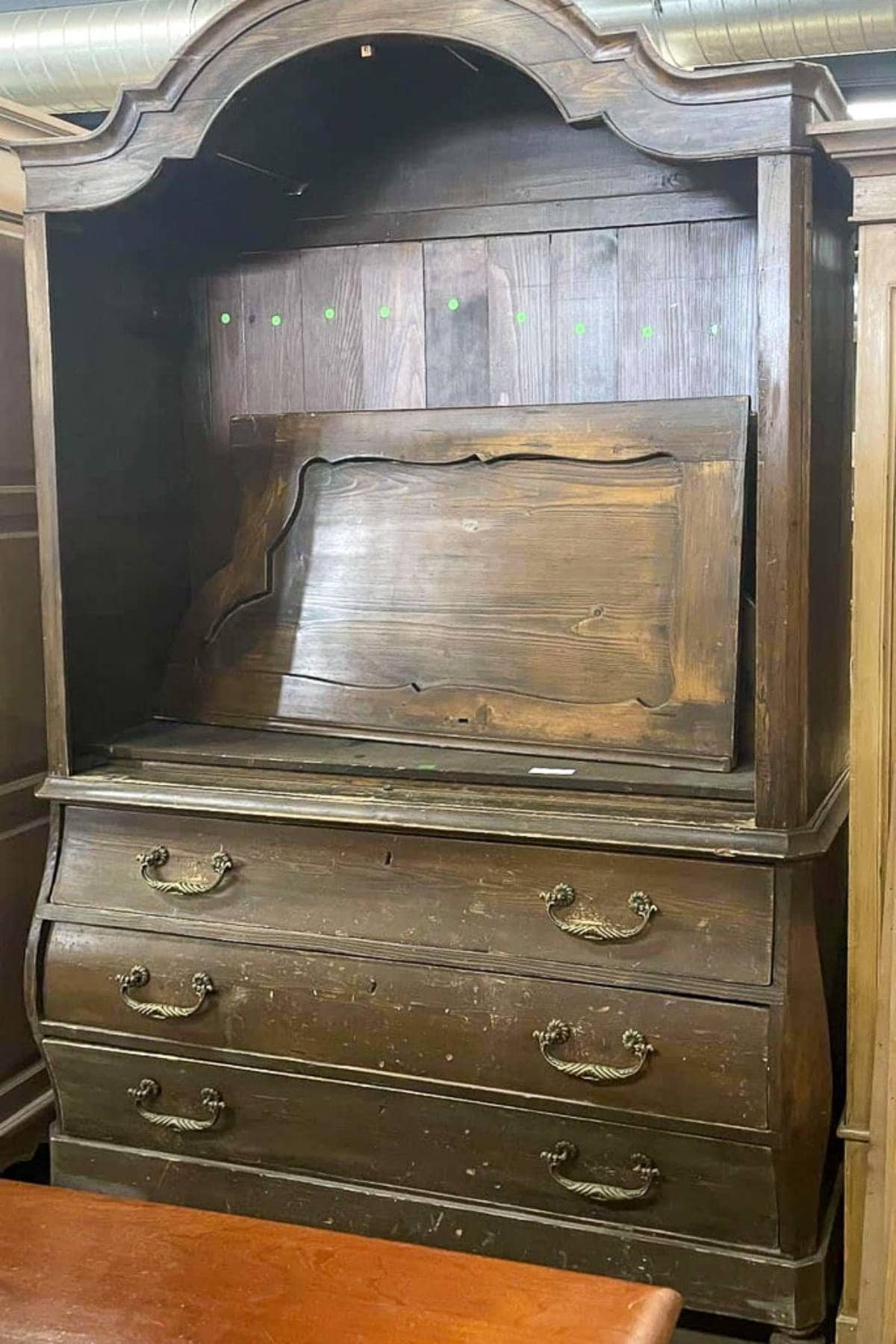 A vintage wooden hutch with multiple drawers and ornate handles. The interior compartment is exposed, revealing a section that appears to be in need of repair. The surface exhibits signs of wear and aged patina.